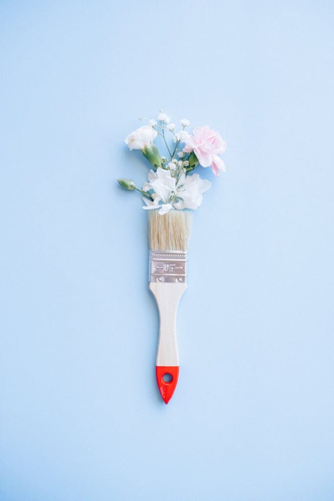 pexels-photo-5642102 A minimalist image of a paintbrush adorned with delicate flowers against a blue background.