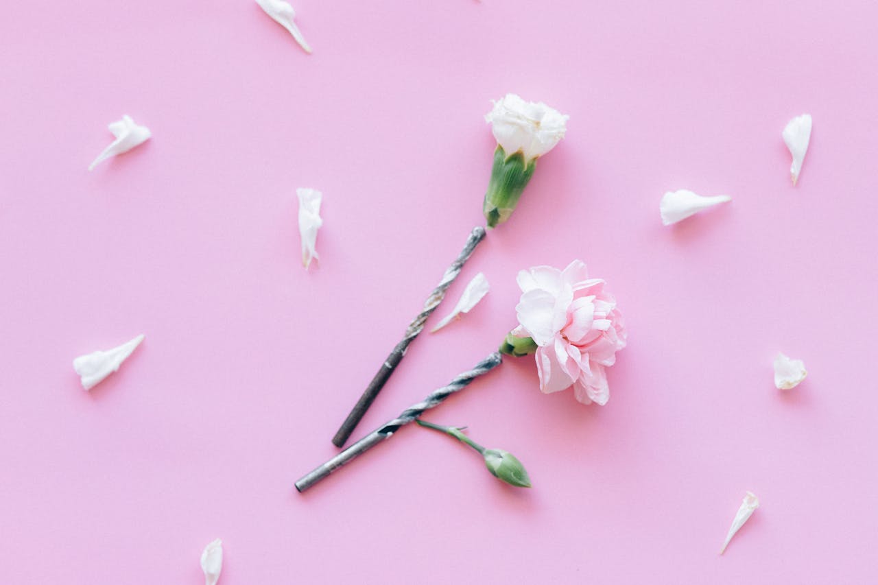 Soft pink flowers and drill bits create an artistic contrast on a pastel pink background.